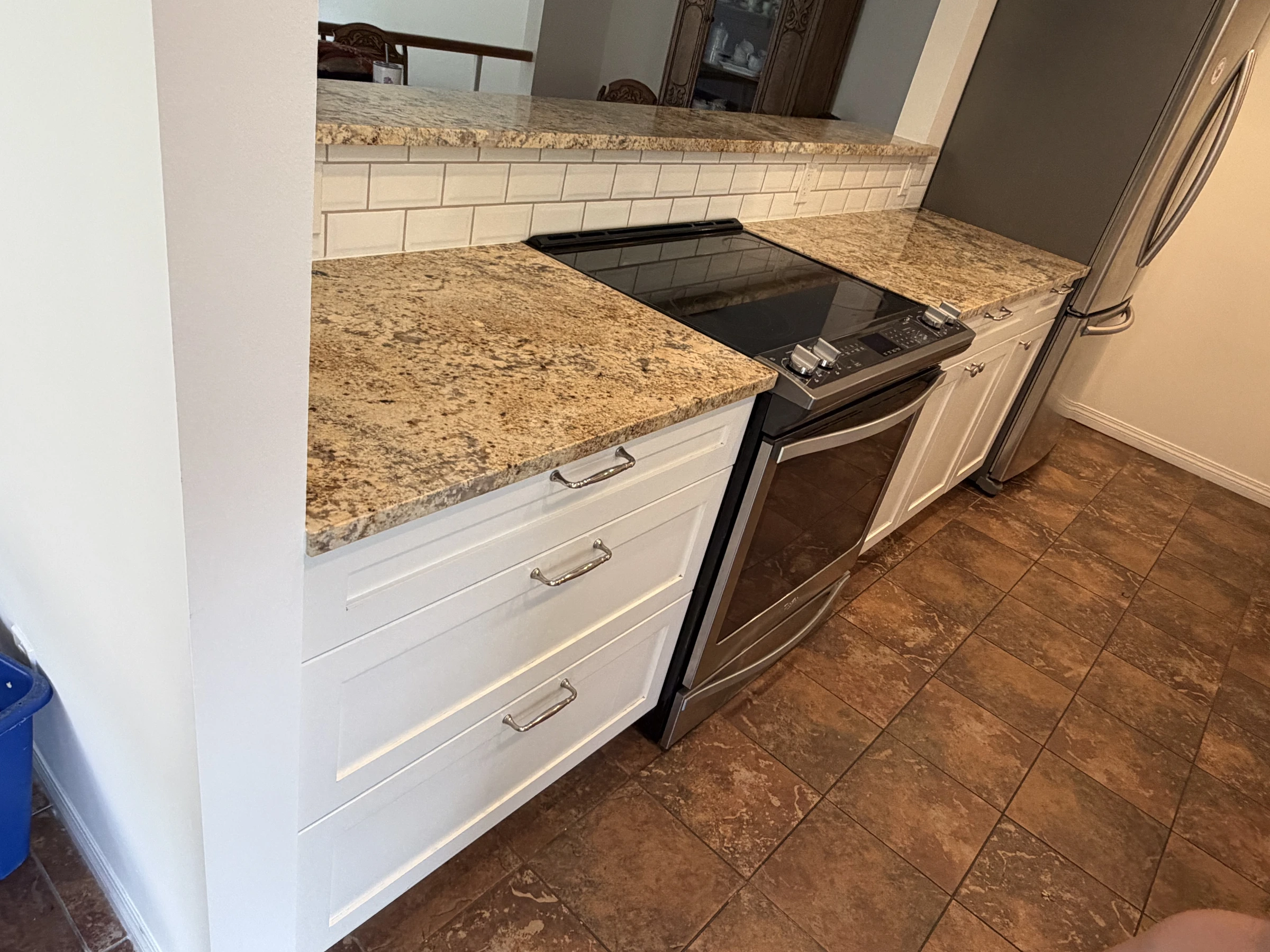 Before photo of white kitchen lower cabinets beside a stove and stone countertop