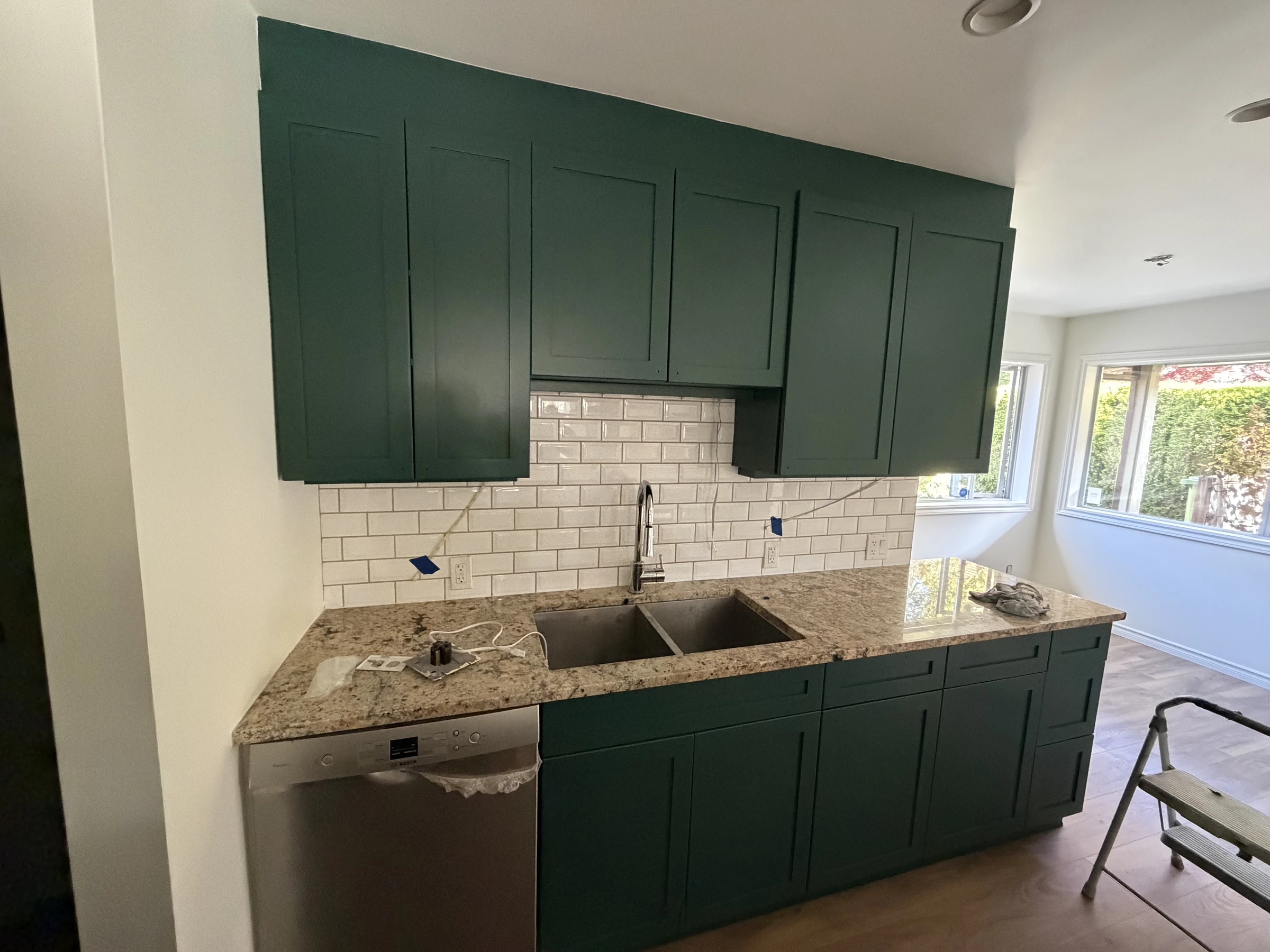 After photo of deep green kitchen cabinets with stone countertop and tiled backsplash