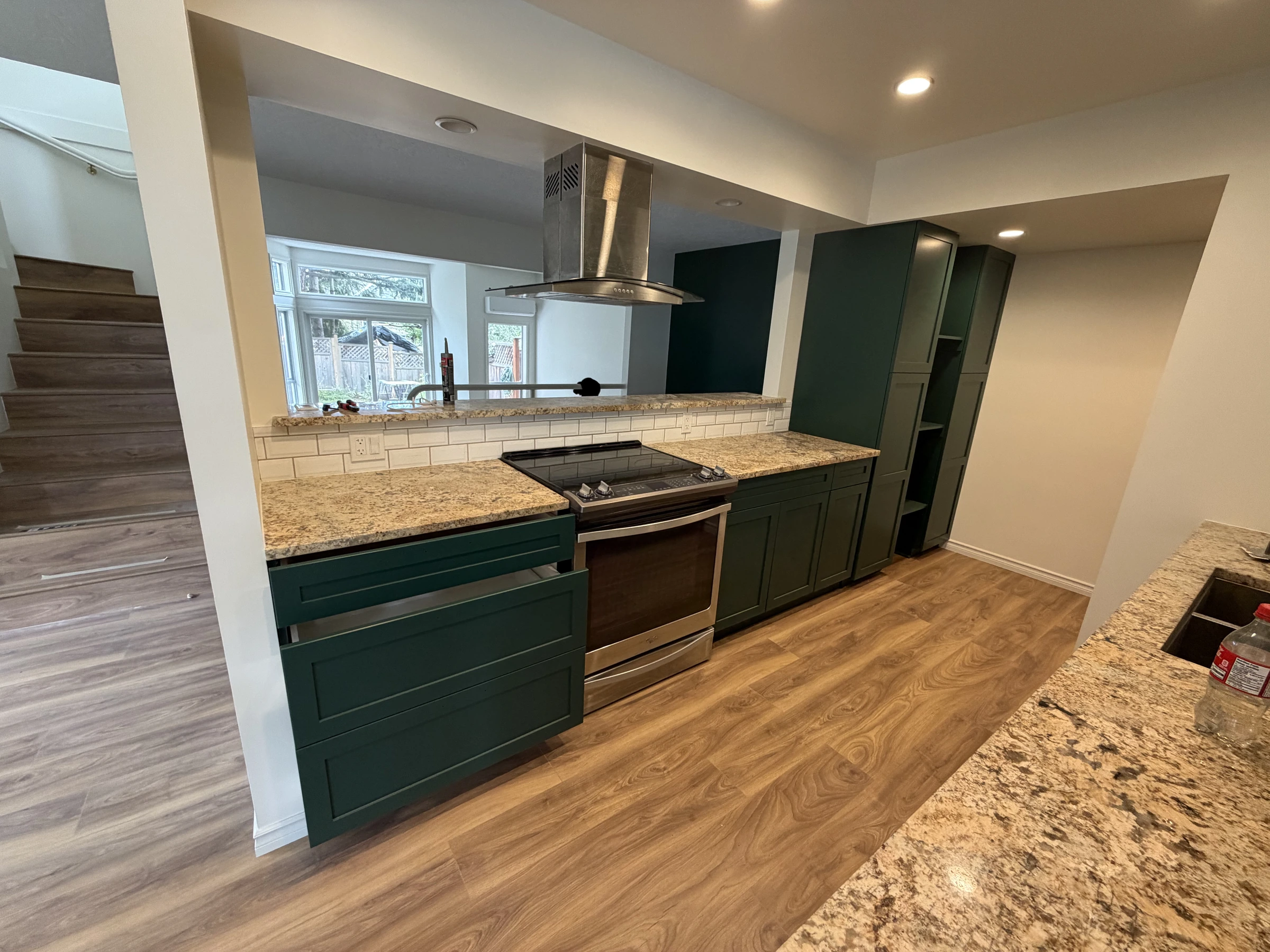 Wide finished kitchen with deep green cabinets, new flooring and adjoining room